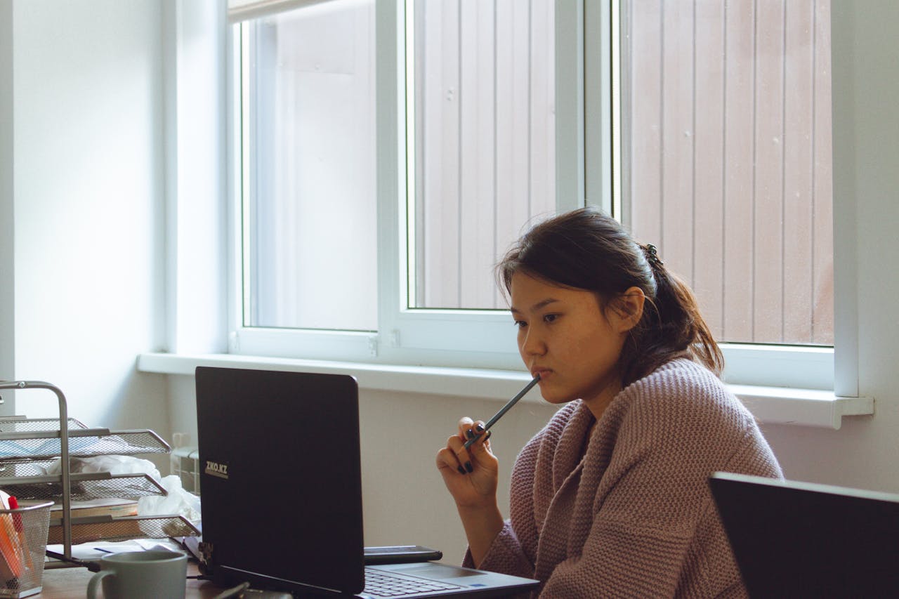 Young woman in cozy sweater working intently on laptop at desk.